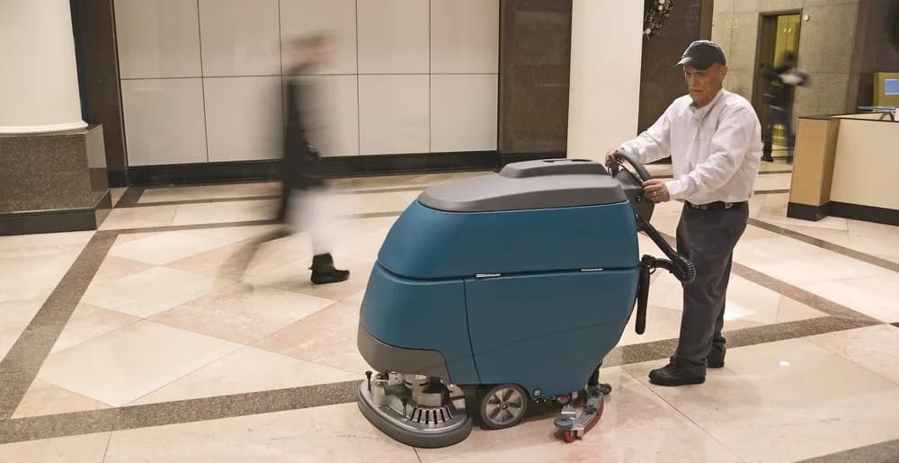 Medewerker reinigt de vloer van een entreehal met een schrobmachine